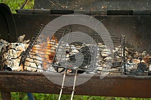 Grill grate is on the burning chargrill with hot charcoals and woods in it.