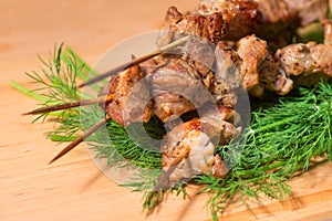 Grill meat on a sticks with green on wooden plate