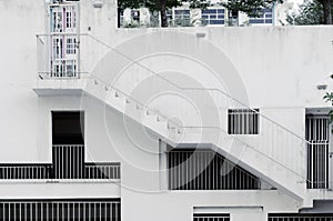 Grille windows of different shapes and sizes at white concrete wall, an external staircase on building, covered parking.
