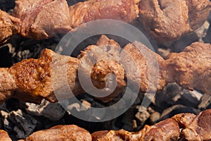 Appetizing juicy pork shish kebabs cooking on metal skewers on charcoal grill with fragrant smoke. Close-up view