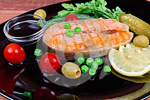 Grilled arctic char steak among vegetables and seasoning on black dish