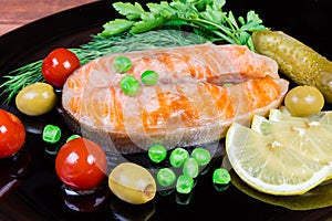 Grilled arctic char among vegetables and greens on black dish