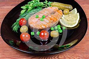 Grilled arctic char among vegetables and greens on black dish