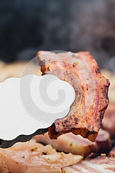 Grilled bacon in metal tongs close up