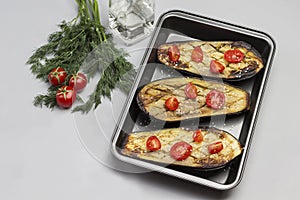 Grilled baked eggplant with tomatoes in pallet. Dill and tomatoes on table