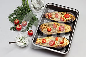 Grilled baked eggplant with tomatoes in pallet. Dill and tomatoes on table. Sauce in glass bowl