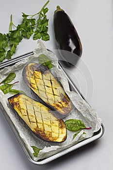 Grilled baked eggplants on pallet. Whole eggplant, onion and parsley on table