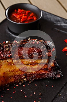 Grilled and barbecue hot pork ribs with hot chilli pepper and hot sauce on black stone background. Isolated. Dish for