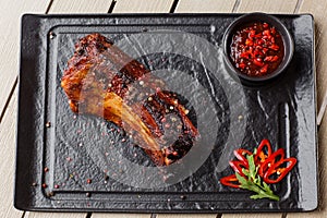 Grilled and barbecue hot pork ribs with hot chilli pepper and hot sauce on black stone background. Isolated. Dish for