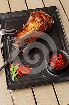Grilled and barbecue hot pork ribs with hot chilli pepper and hot sauce on black stone background. Isolated. Dish for