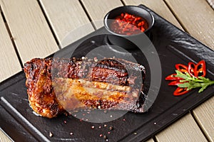 Grilled and barbecue hot pork ribs with hot chilli pepper and hot sauce on black stone background. Isolated. Dish for