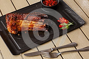 Grilled and barbecue hot pork ribs with hot chilli pepper and hot sauce on black stone background. Isolated. Dish for