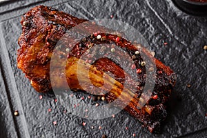 Grilled and barbecue hot pork ribs with hot chilli pepper and hot sauce on black stone background. Isolated. Dish for