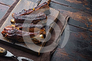 Grilled barbecue pork ribs, on wooden serving board, with barbeque knife and meat fork, on old dark  wooden table background