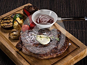 Grilled beef angus steak with melted butter on a wooden cutting board served with grilled vegetables, close up photo on a dark