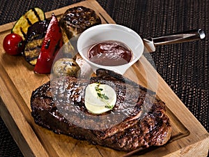 Grilled beef angus steak with melted butter on a wooden cutting board served with grilled vegetables, close up photo on a dark