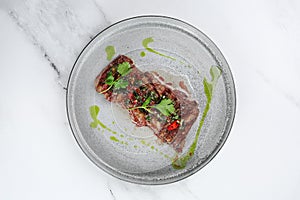 Grilled beef chuck steak top view. sliced steak with chili pepper and green on light marble background with copy space