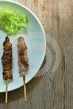 Grilled beef meat dressings spicy sauce stabbing in wooden stick with vegetable on plate