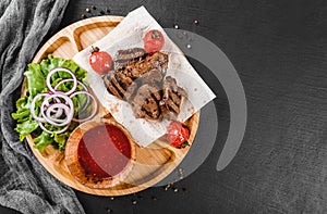 Grilled beef meat and vegetables with fresh salad and bbq sauce on cutting board over black stone background. Hot Meat Dishes