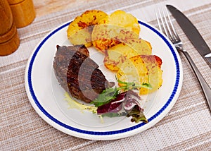 Grilled beef steak with baked potato slices garnished with greens