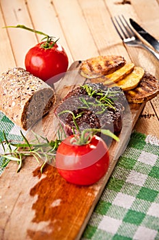 Grilled beef steak, baked potatoes and vegetable on wooden bread