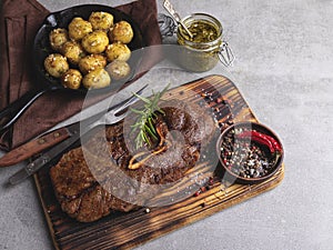 Grilled beef steak with bone on a cutting board, roasted new potatoes in a pan
