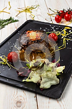 Grilled beef steak with butter, spices, mix salad and cherry tomatoes on black stone cutting board, lunch menu of national food