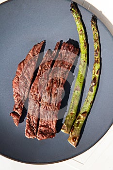 Grilled beef steak with Green asparagus on blue plate and white background top view, barbecue dry aged steak