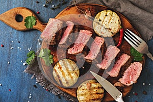 Grilled beef steak medium rare is sliced on a cutting board with spices and baked eggplants. Top view, flat lay. Toned