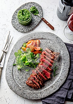 Grilled beef steak medium rare slices on gray stone plate with salad and chimichurri sauce