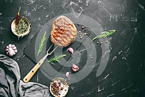 Grilled beef steak with rosemary and spices on a black stone background. Top view, flat lay, copy space. Photo toned