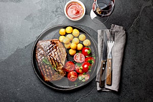 Grilled beef steak served on cast iron plate with tomato salad, potatoes balls and red wine. Barbecue, bbq meat beef