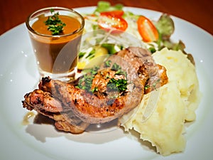 Grilled beef steak sirloin with gravy sauce in small glass, mashed potatoes and vegetable salad on white dish