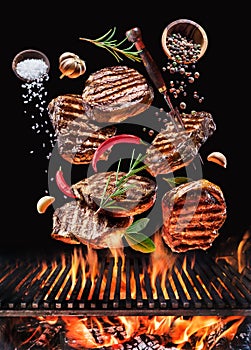 Grilled beef steaks with vegetables and spices fly over the glowing grill barbecue fire