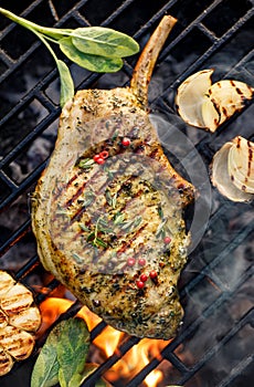Grilled bone-in pork chop, pork steak, tomahawk in a herb marinade on a flaming grill, close-up, top view.