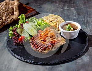 Grilled Boneless Chicken Steak with chili sauce, salad, noodles in dish side view on dark background