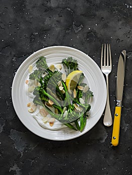 Grilled broccolini with greek yogurt and toasted almonds on a dark background. Delicious breakfast, brunch, snack, appetizer