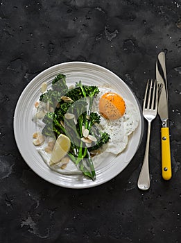 Grilled broccolini with greek yogurt and toasted almonds and fried egg on a dark background. Delicious breakfast, brunch