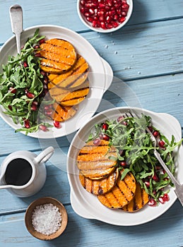 Grilled butternut squash, arugula and pomegranate salad on a blue wooden table, top view. Clean, organic, seasonal, vegetarian foo