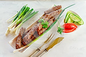 Grilled Cevapcici is a Balkan national dish. Close the row of fried beef kebabs on a white rectangular dish with vegetables