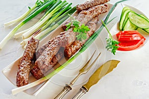 Grilled Cevapcici is a Balkan national dish. Close the row of fried beef kebabs on a white rectangular dish with vegetables