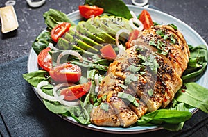 Grilled chicken breast and avocado salad with spinach and cherry tomatoes on black stone background. Healthy food, ketogenic diet