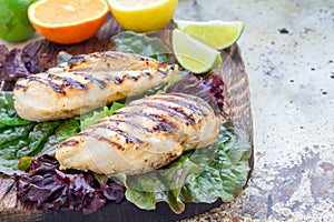 Grilled chicken breast in citrus marinade on salad leaves and wooden board, horizontal, copy space