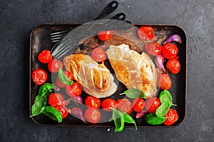 Grilled chicken breast fillet with young garlic, cherry tomatoes on a baking sheet with basil leaves. Geared dish on a