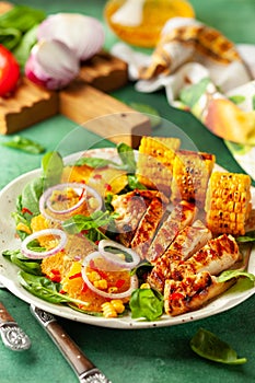 Grilled chicken breasts cooked on a BBQ served with citrus salad and corn on a plate. Close up view. Concept homemade summer