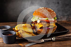 Grilled chicken burger with double cutlet, cheese and fries in a metal bowl on a wooden table
