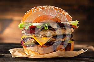 Grilled chicken burger with double cutlet, cheese and vegetables on a wooden table.