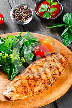 Grilled chicken fillet with fresh vegetable salad, tomatoes and sauce on wooden cutting board