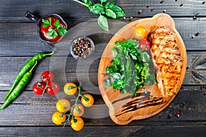 Grilled chicken fillet with fresh vegetable salad, tomatoes and sauce on wooden cutting board. Hot Meat Dishes.