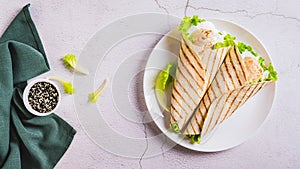 Grilled chicken fillet wrapped in tortilla with lettuce and sauce on a plate top view web banner